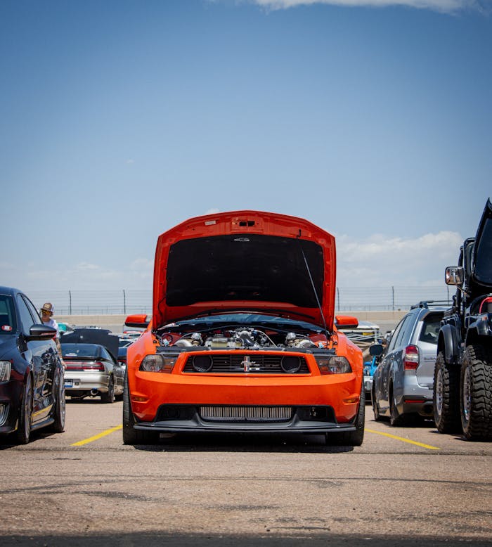Front view of a red Mustang with the hood open at an outdoor car show.