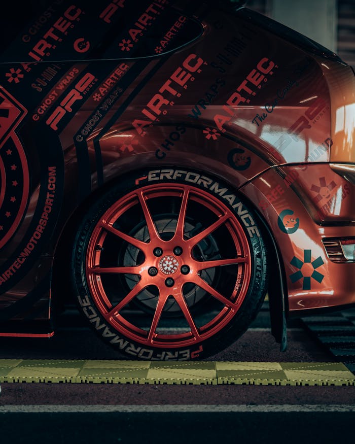 Close-up of a custom red sports car featuring striking graphics and performance wheels under soft lighting.